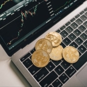 Bitcoin coins on a laptop keyboard with a crypto market chart, symbolizing the need for the Voluntary Disclosure Programme for crypto traders.