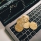 Bitcoin coins on a laptop keyboard with a crypto market chart, symbolizing the need for the Voluntary Disclosure Programme for crypto traders.